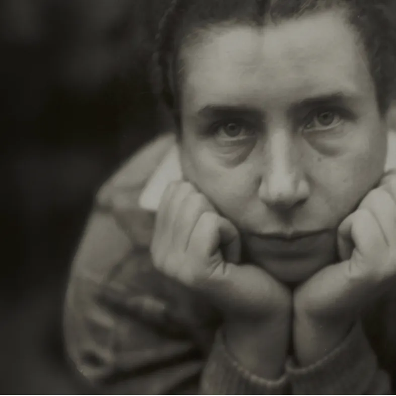 Portrait en noir et blanc de Lucia Moholy, photographe du Bauhaus, le visage posé sur ses mains, regard direct vers l’objectif